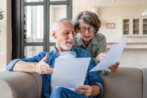 Husband And Wife Reviewing Reverse Mortgage Document Learning About How They Retain Home Ownership After The Loan